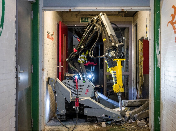 Demolition robot being demonstrated inside a building hallway.